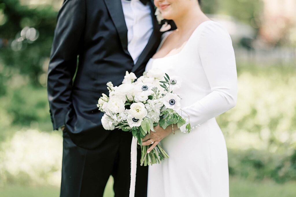 Bride and groom in park holding white wedding bouquet