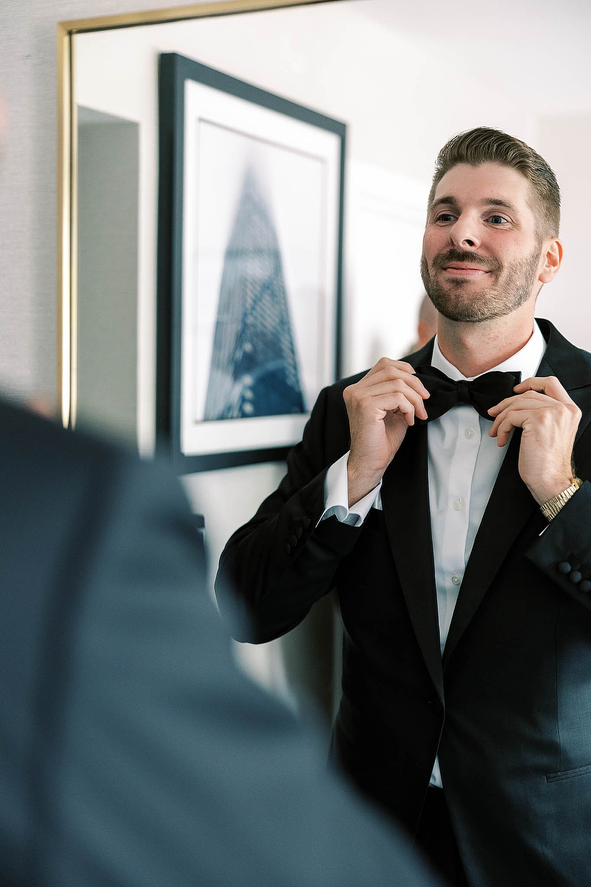 Groom fixing his bowtie in mirror at Claridge House Hotel