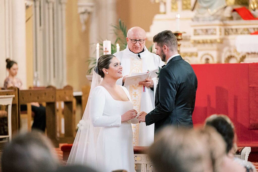 Bride and groom exchange vows with priest in background