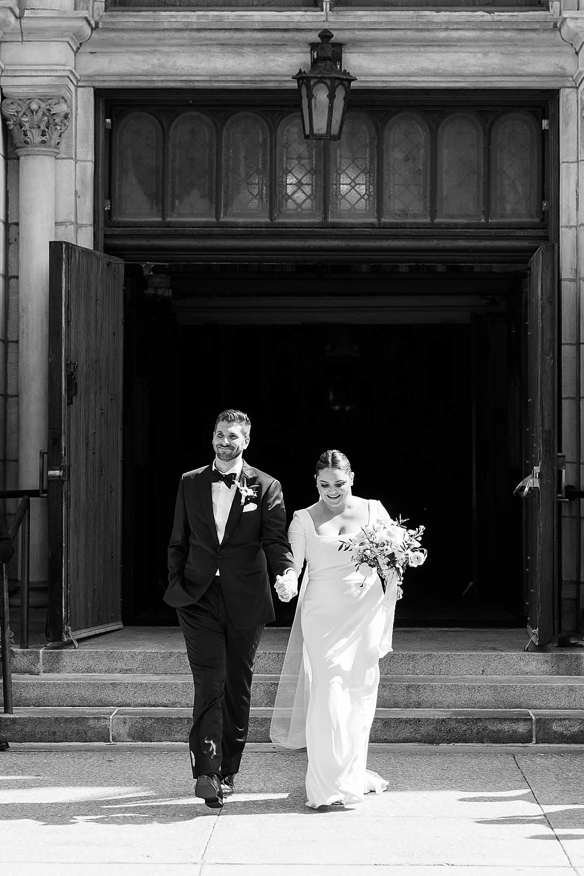 Black and white photo of bride and groom leaving church after wedding