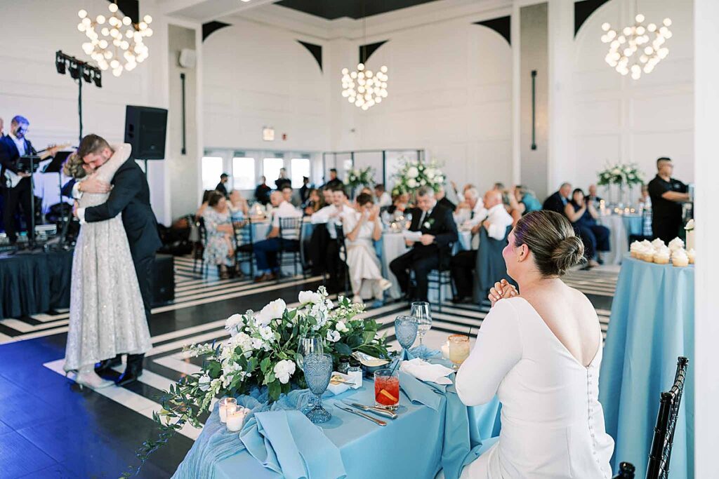 Bride in white dress watches man in suit and mom dance