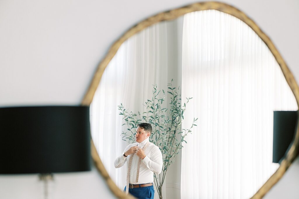 Photo of groom tying his tie through a mirror