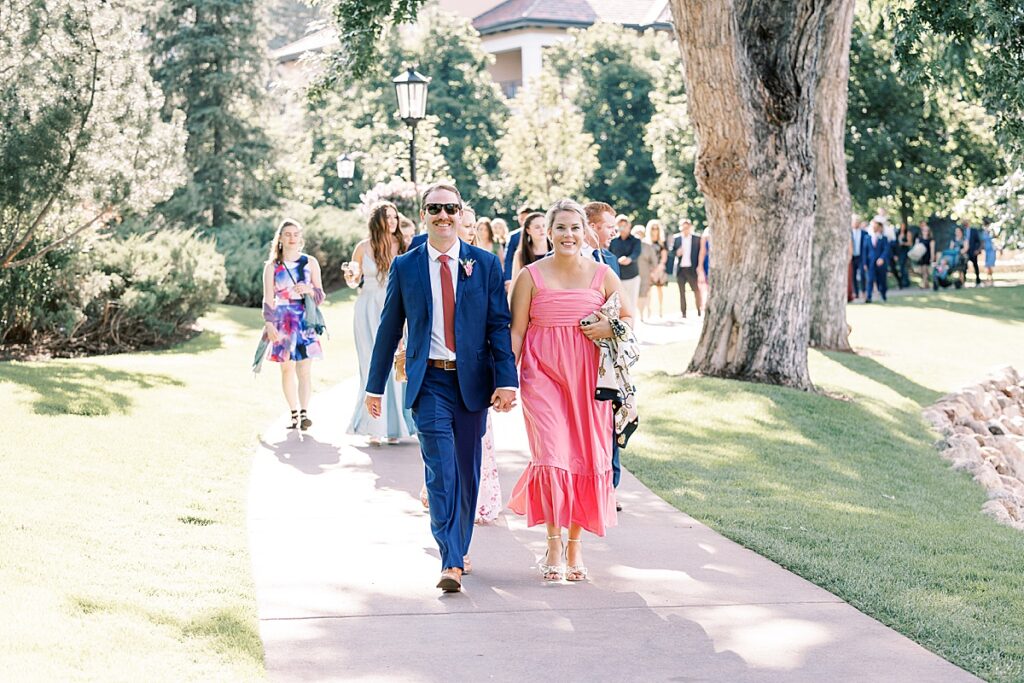 Wedding guest in pink dress walking on concrete path under trees