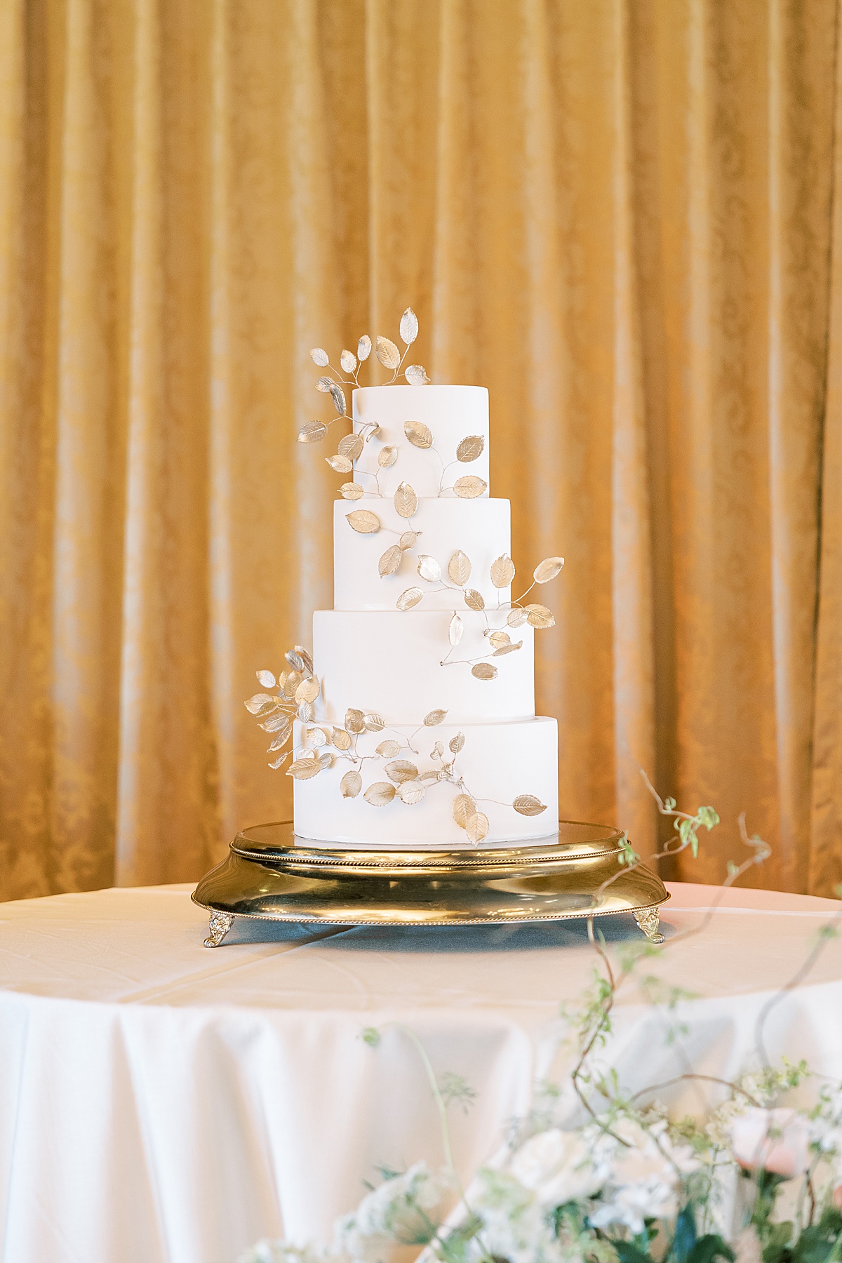 White wedding cake with gold leaves against a gold background