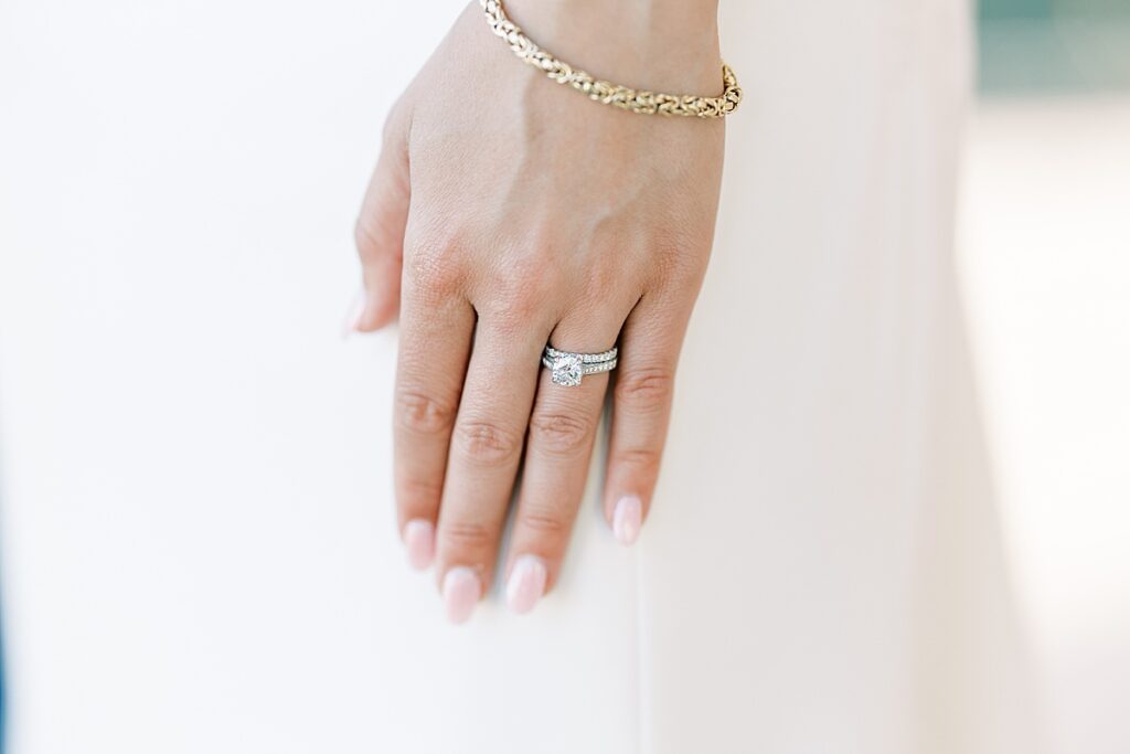 Wedding rings on woman's hand resting against wedding dress