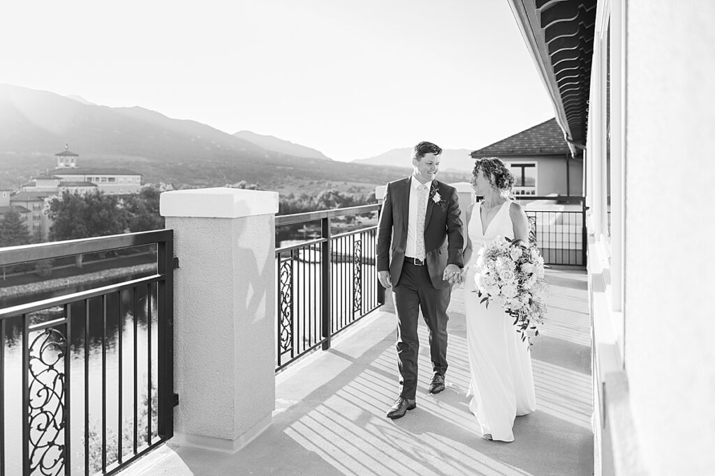 Black and white image of bride and groom walking on balcony at the Broadmoor