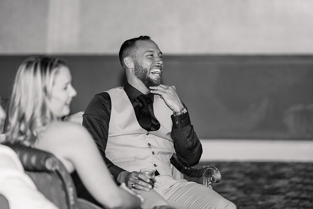 Wedding guest in black shirt and gray vest laughing