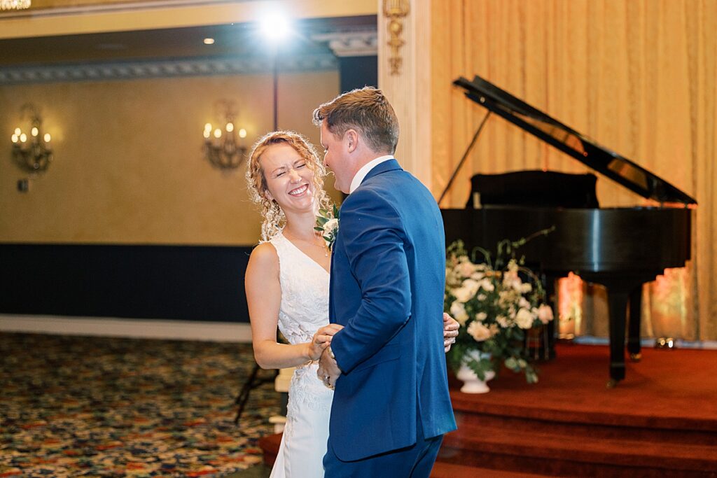 Bride smiling with grand piano in the background dancing with groom in blue suit