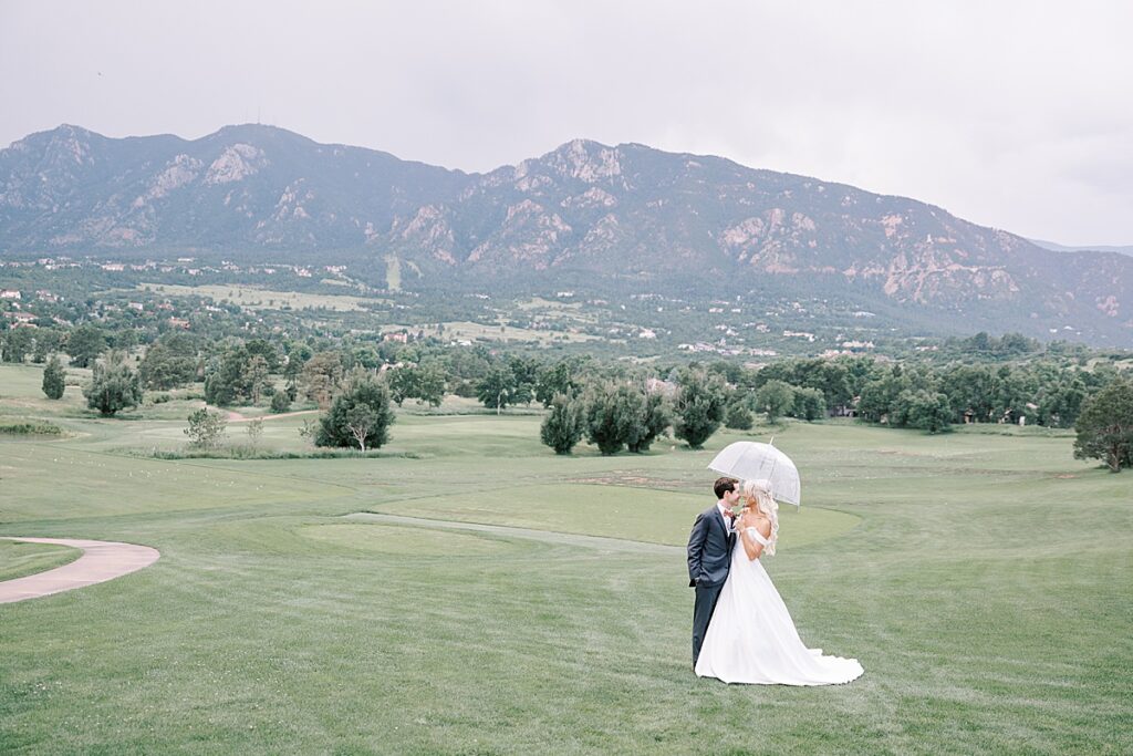 Bride and groom posing with an umbrella in front on mountains