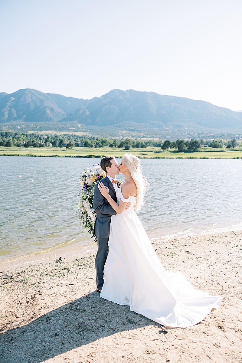 Bride and groom kissing on a beach in front of mountains