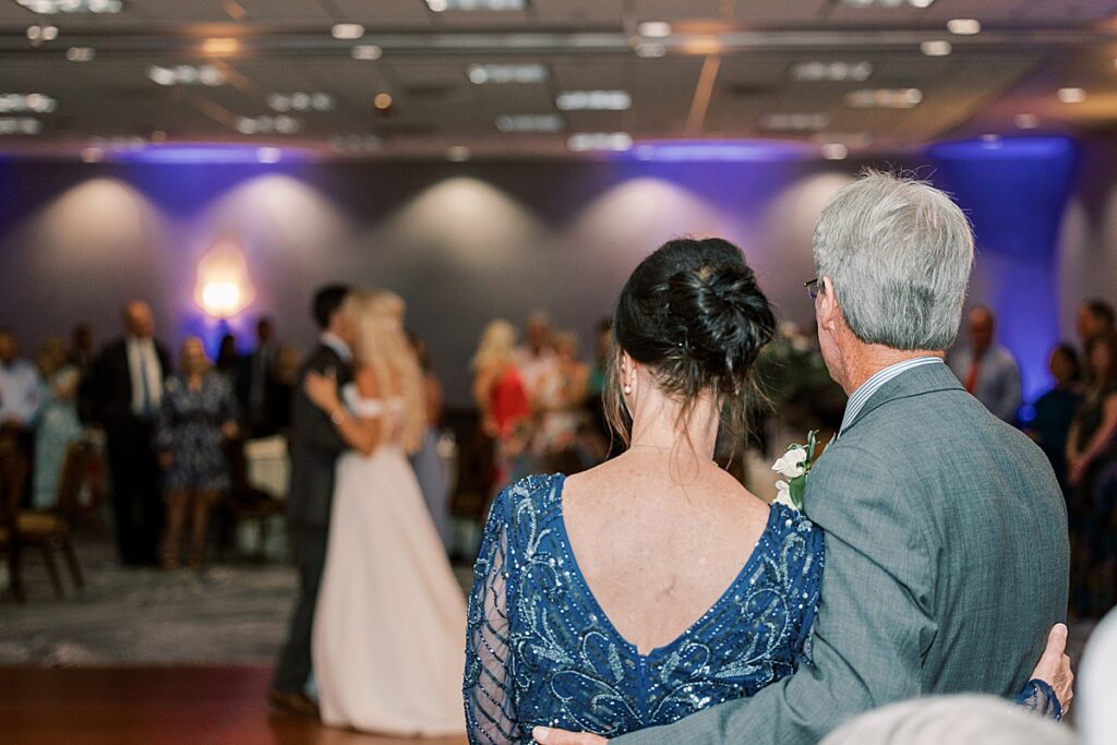 Man in gray suit and woman in blue dress watching wedding couple dancing