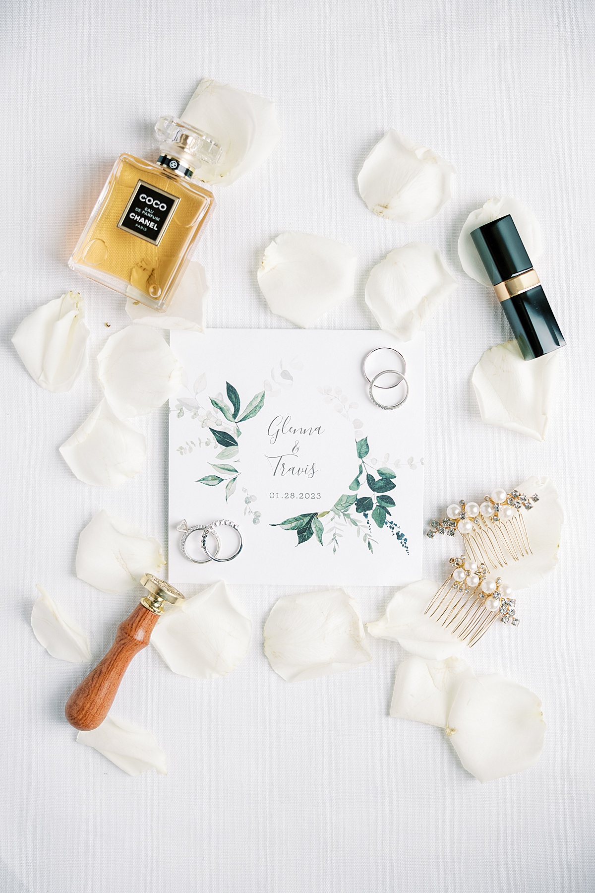 Wedding invitation surrounded by lipstick, rose petals and other accessories