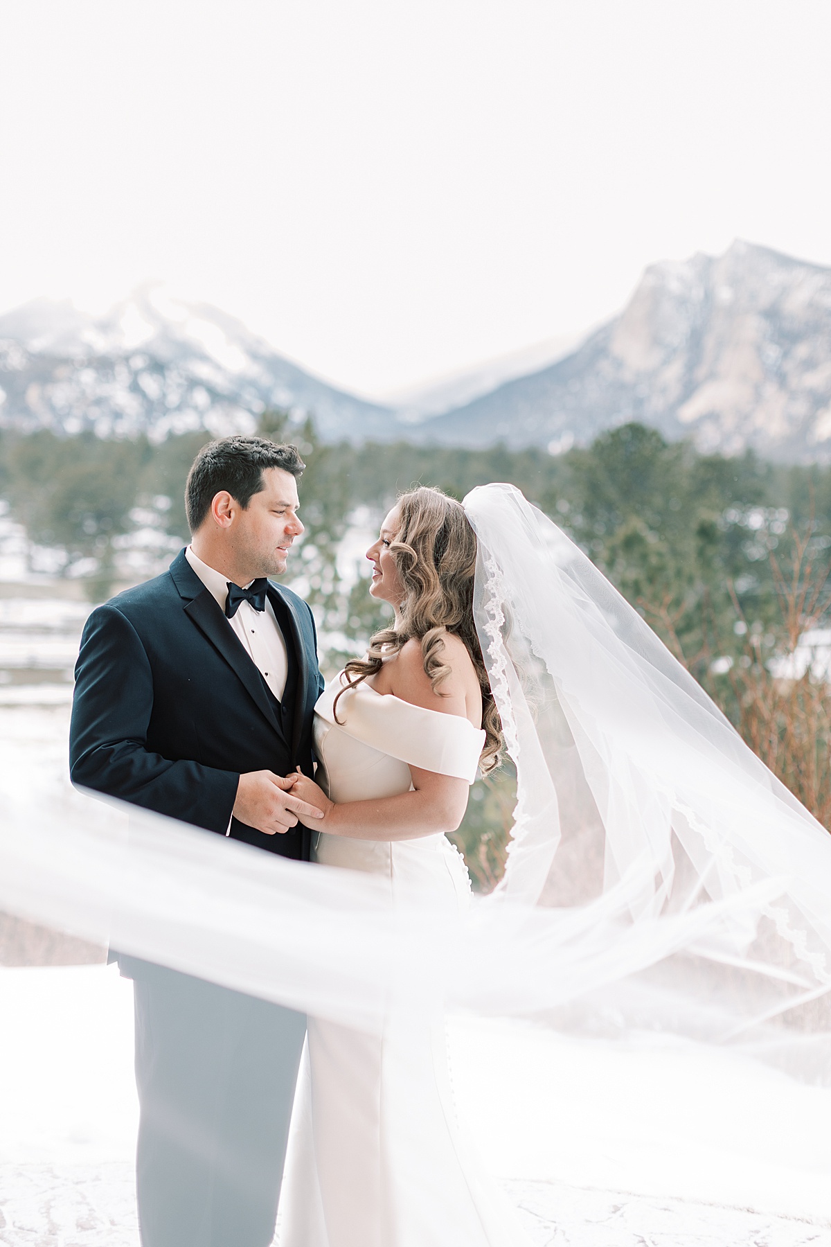 Bride and groom standing in snow smiling at each other