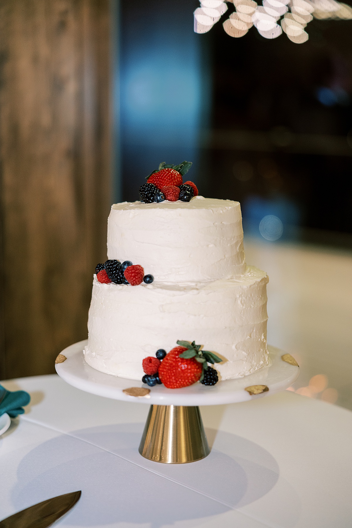 White wedding cake on gold cake stand with strawberries and blueberries