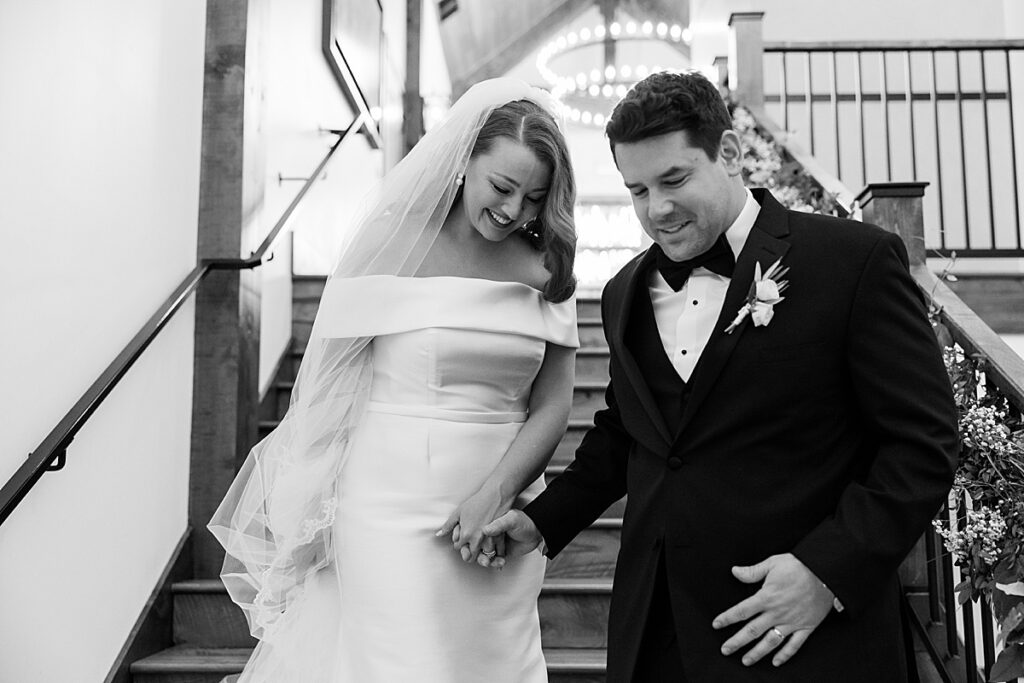 Bride and groom looking down and holding hands walking down stairs