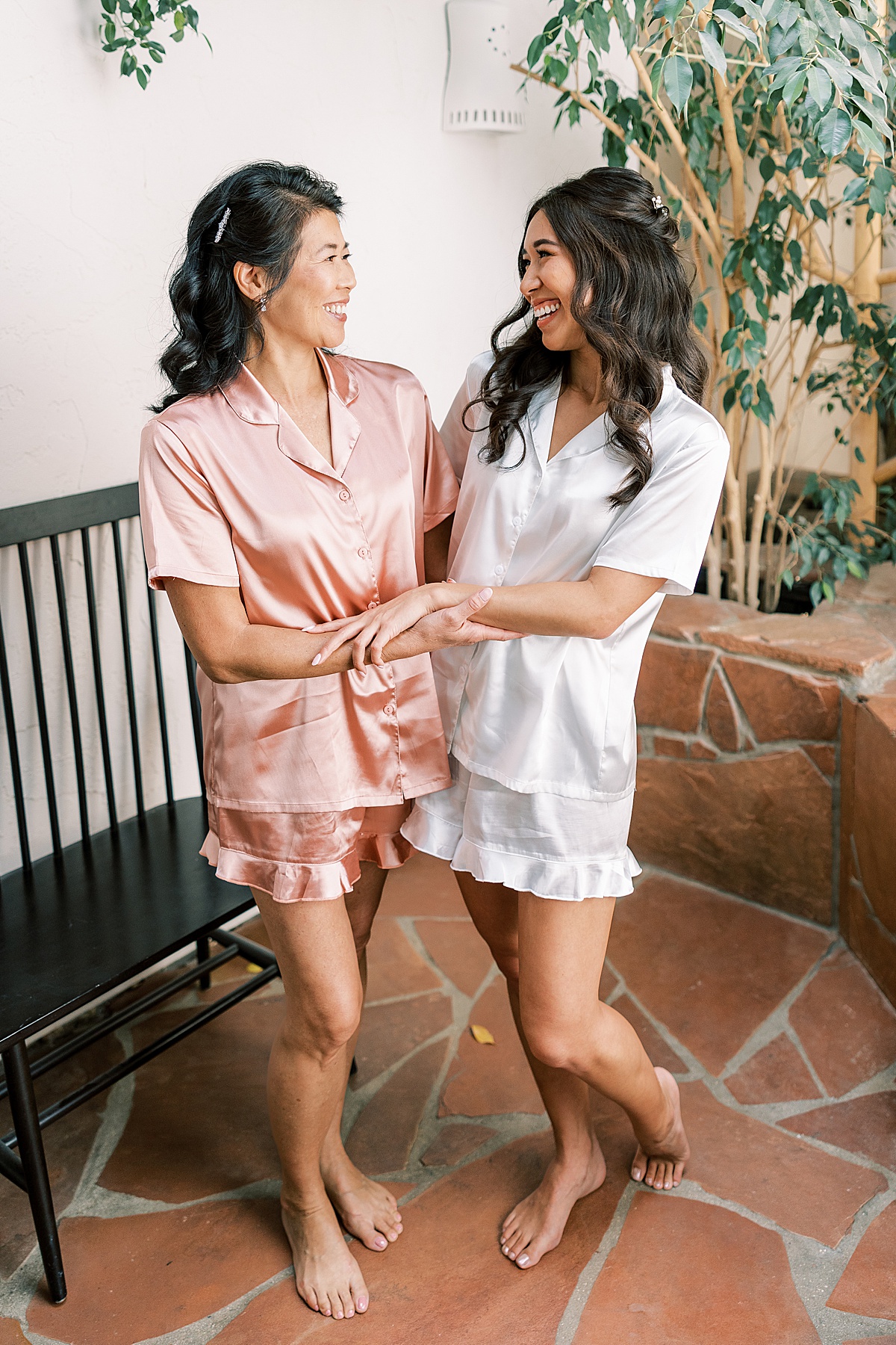 Bride in white robe posing with arms around mom in pink robe