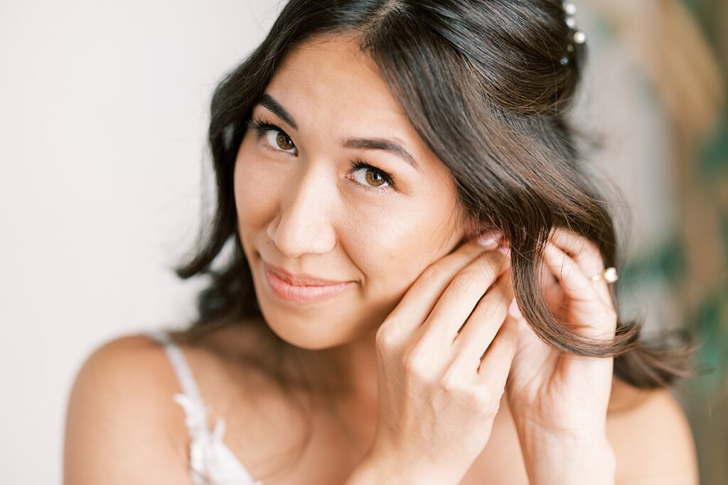 Bride looking at camera while putting in earrings