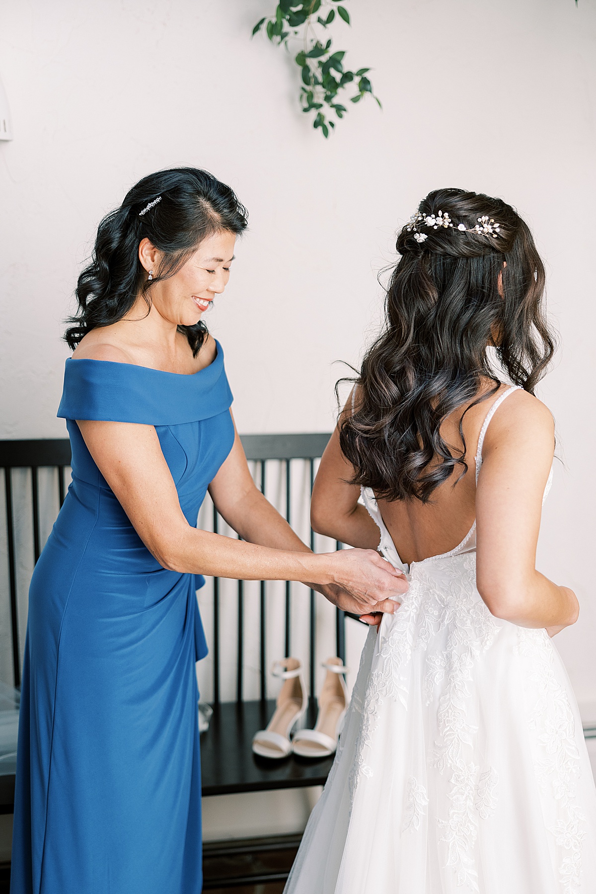 Woman in blue dress zipping up bride's white dress