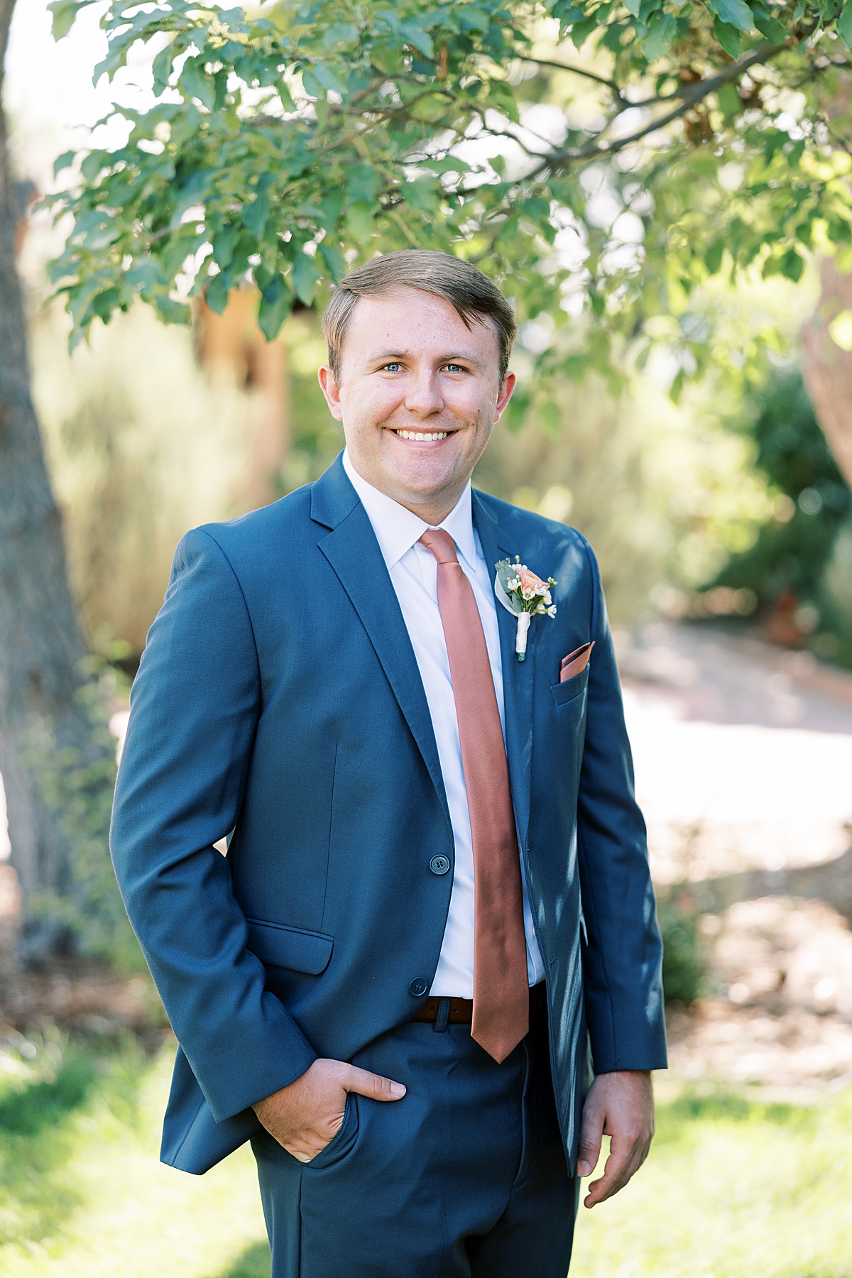 Groom posing with his hand in pocket in front of trees in blue suit