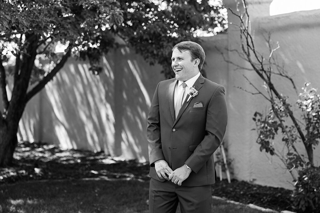 Black and white photo of a man in suit smiling during his wedding