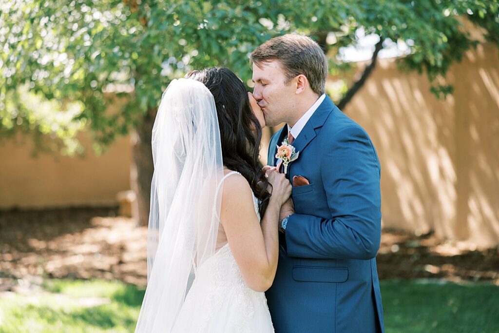 Bride in white dress and groom in blue suit kissing during their first look