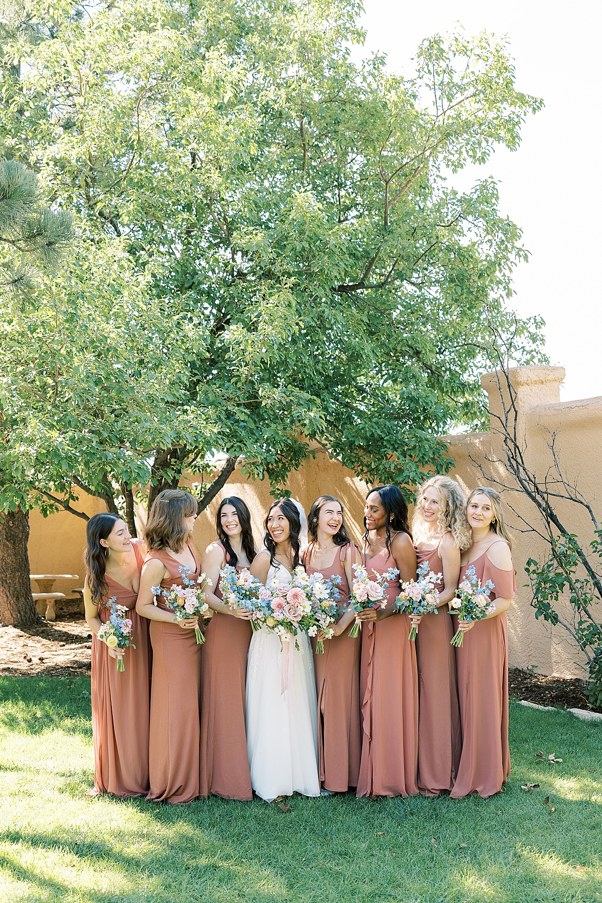 Bridal party in salmon colored dresses laughing at each other