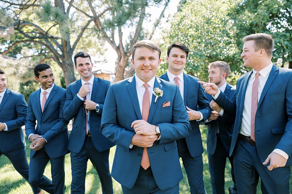 Groom in blue suit looking at camera while his groomsmen walk behind him 