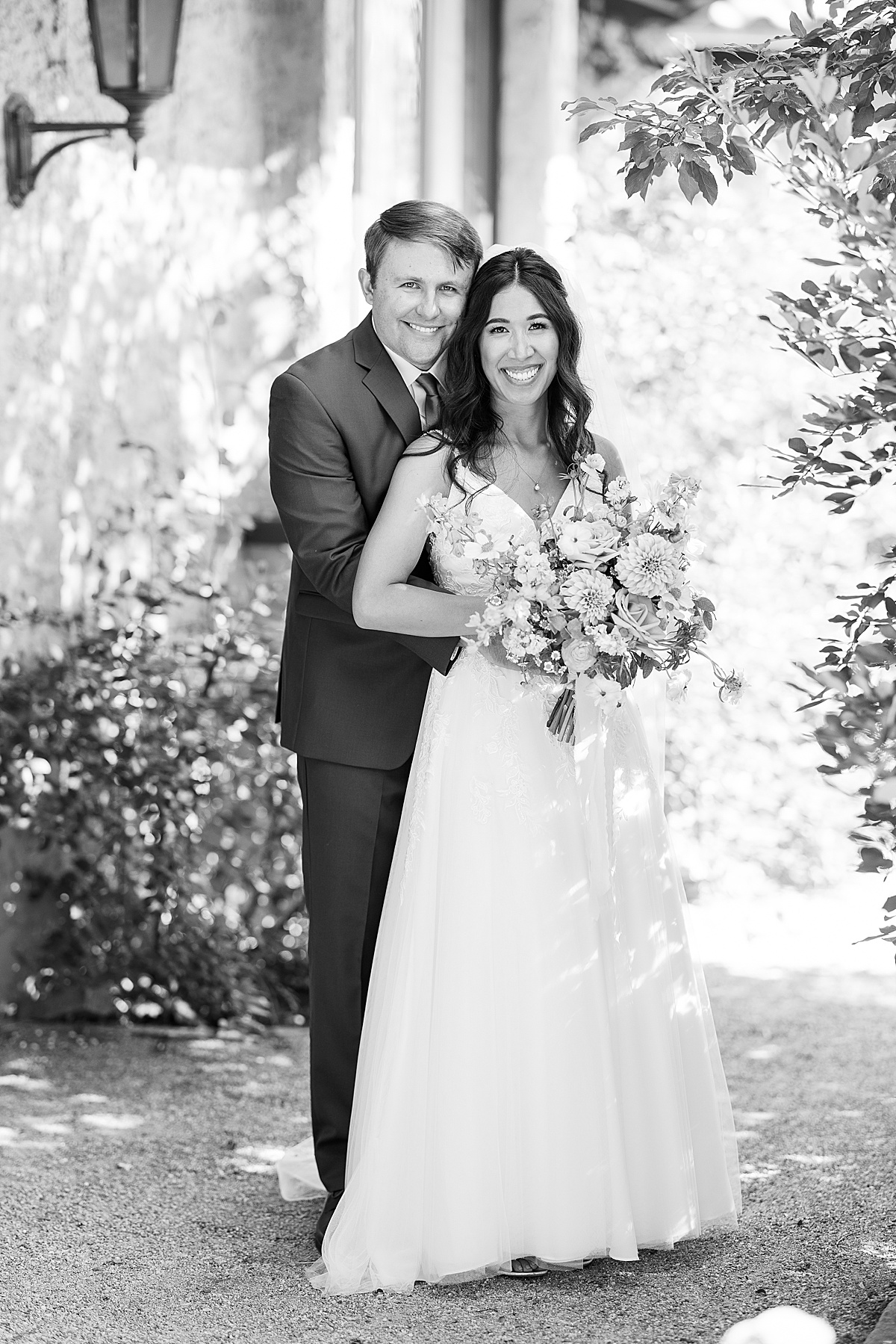 Black and white photo of a groom behind bride smiling at camera