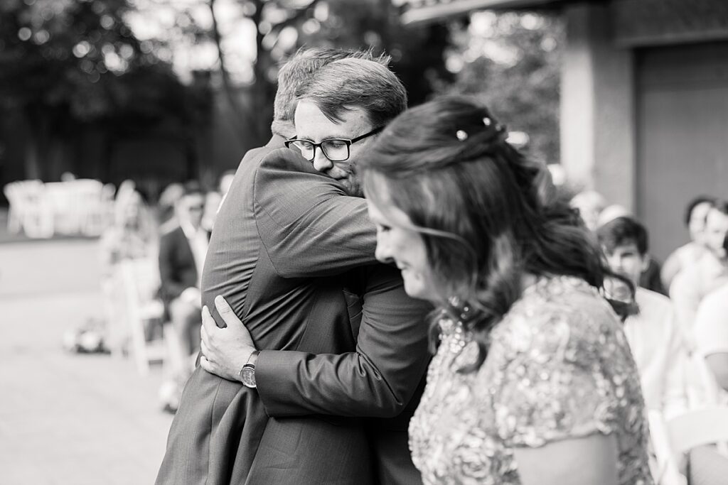 Black and white photo of groom in glasses hugging father