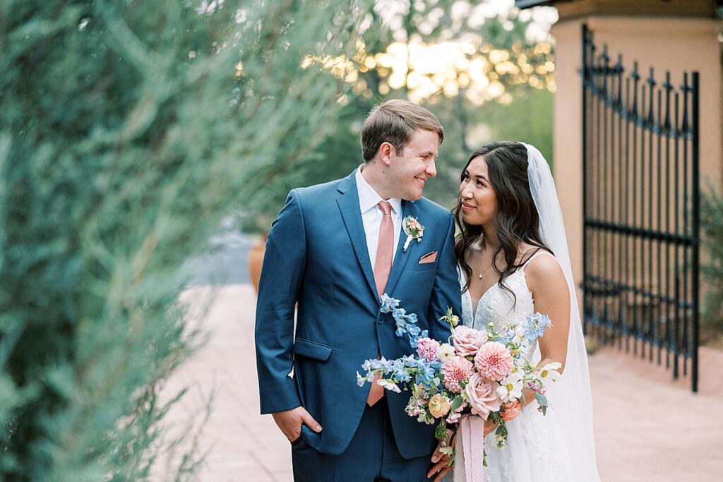 Bride and groom standing in front of gate arm in arm for wedding photo