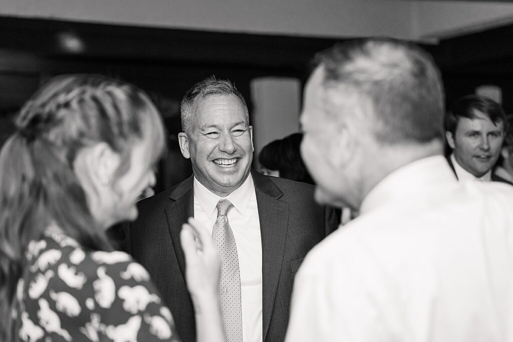 Black and white photo of man laughing at wedding guests