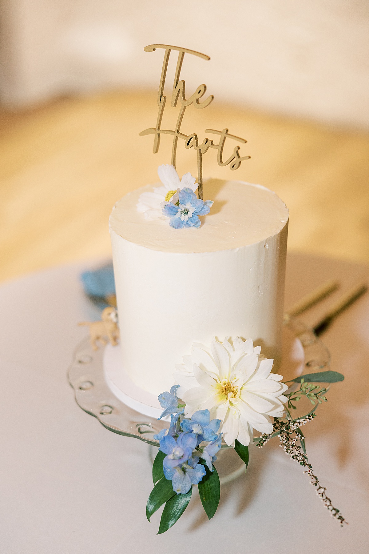 White wedding cake with blue and white flowers and "The Harts" written on the top