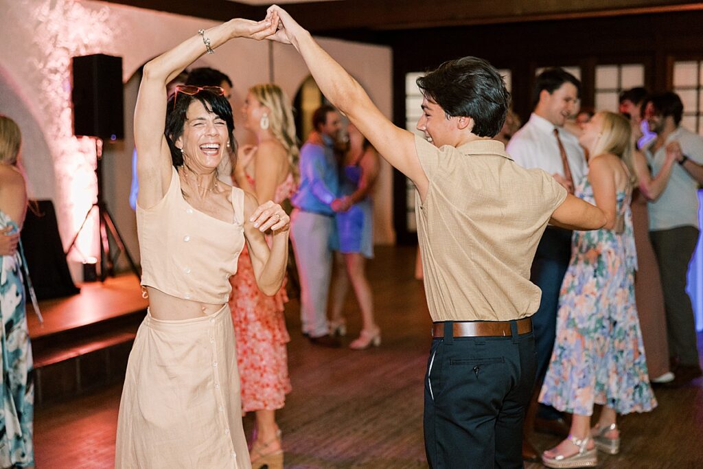 Wedding guest in light colored dress dancing with her arms up