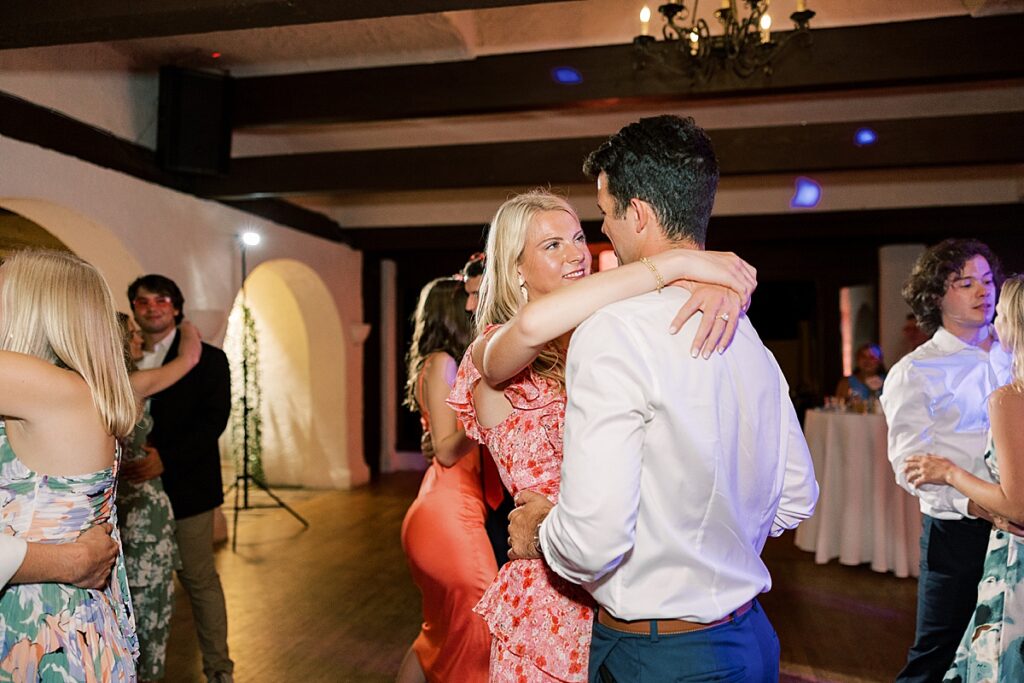 Guest in pink dress dances with her arms around a man in a white shirt