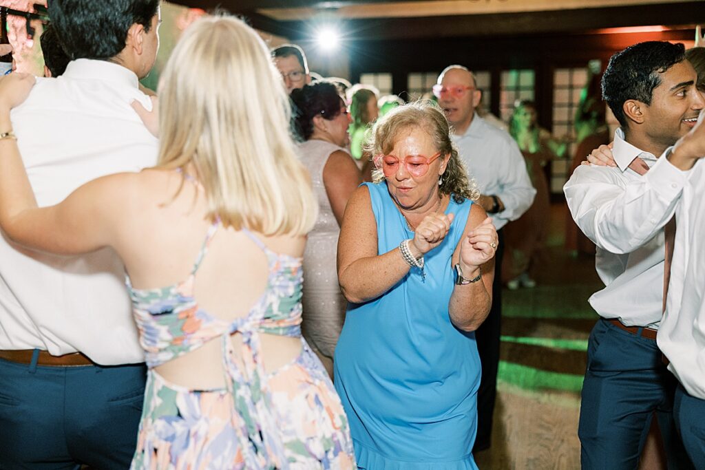 Wedding guest in blue dress and pink glasses dancing