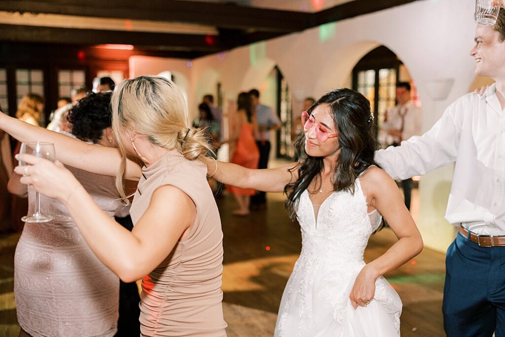 Bride in pink sunglasses dancing in a wedding guest train