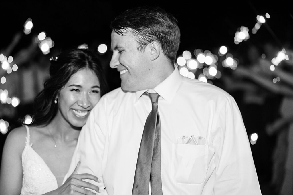 Black and white photo of groom looking down at bride during sparkler exit