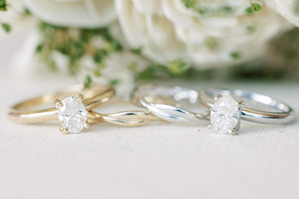 Two oval shaped engagement rings sitting in front of wooden flowers