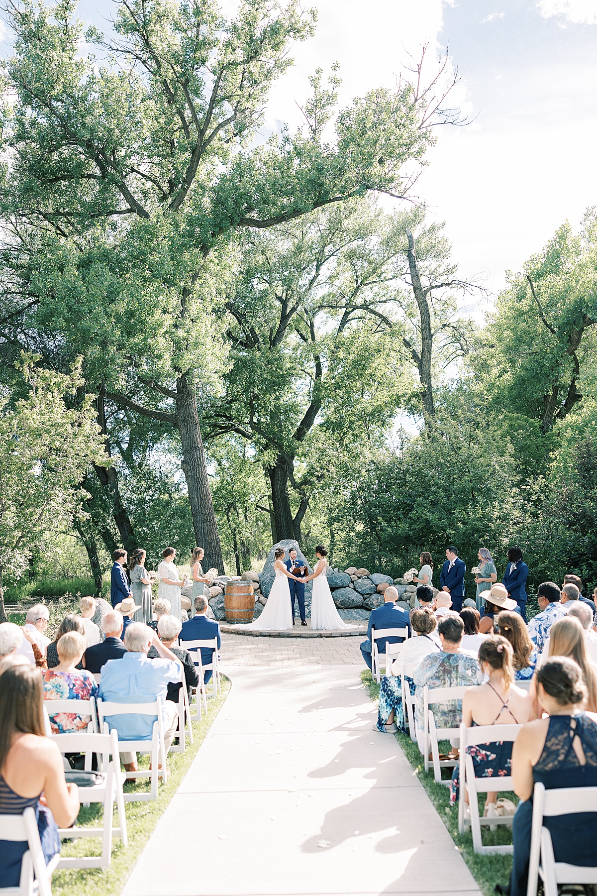 Photo of wedding ceremony for two brides standing in front of large trees