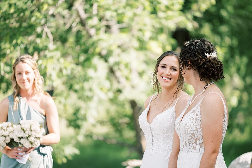 Woman looking at another woman during their wedding ceremony in front of green trees