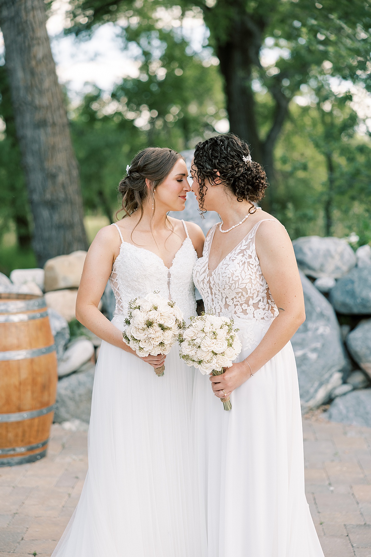 Two brides posing forehead to forehead holding wooden flowers