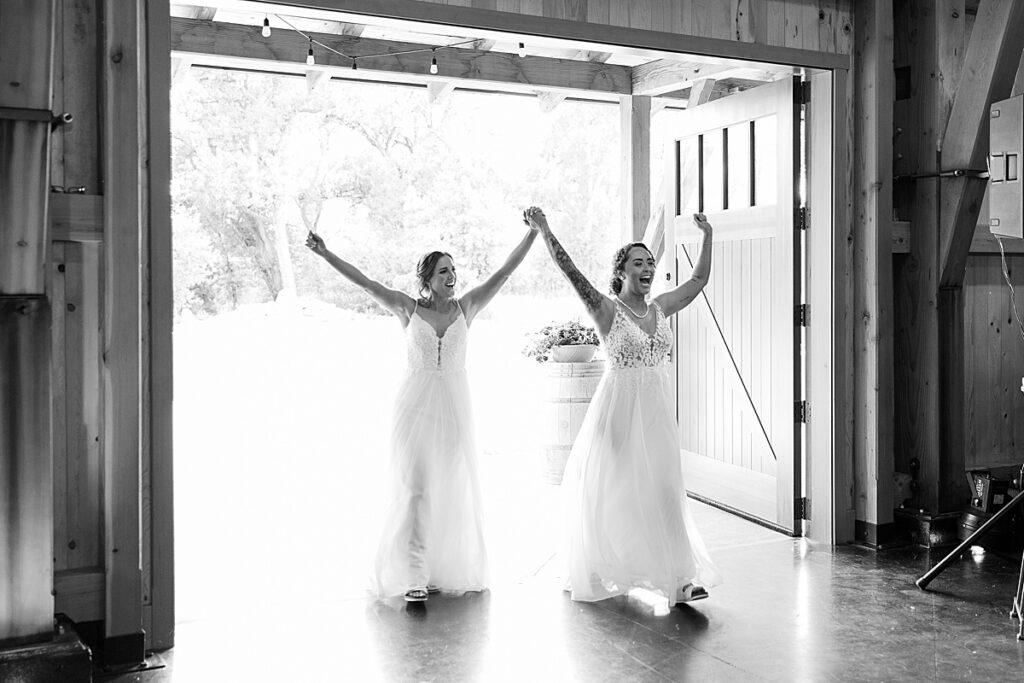 Brides walking into a room holding hands above their heads cheering