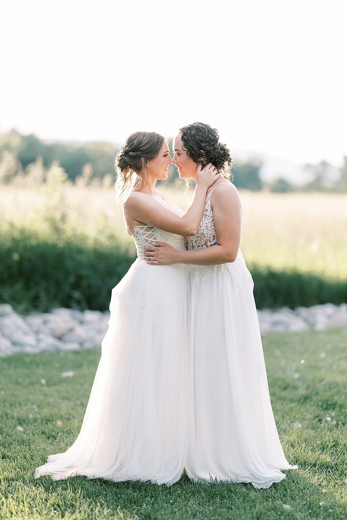 Two brides standing chest to chest in grass