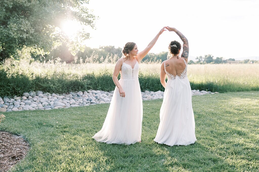 Bride twirling other bride around on grass field