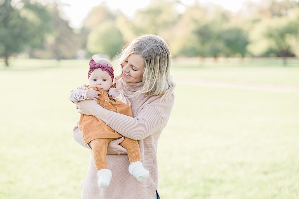 Woman in pink sweater holding baby in orange clothes and pink headband