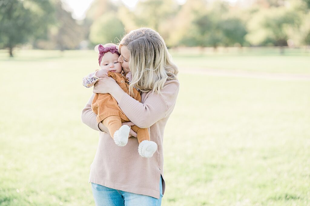 Woman in pink sweater holding a baby in orange jumpsuit and pink headband