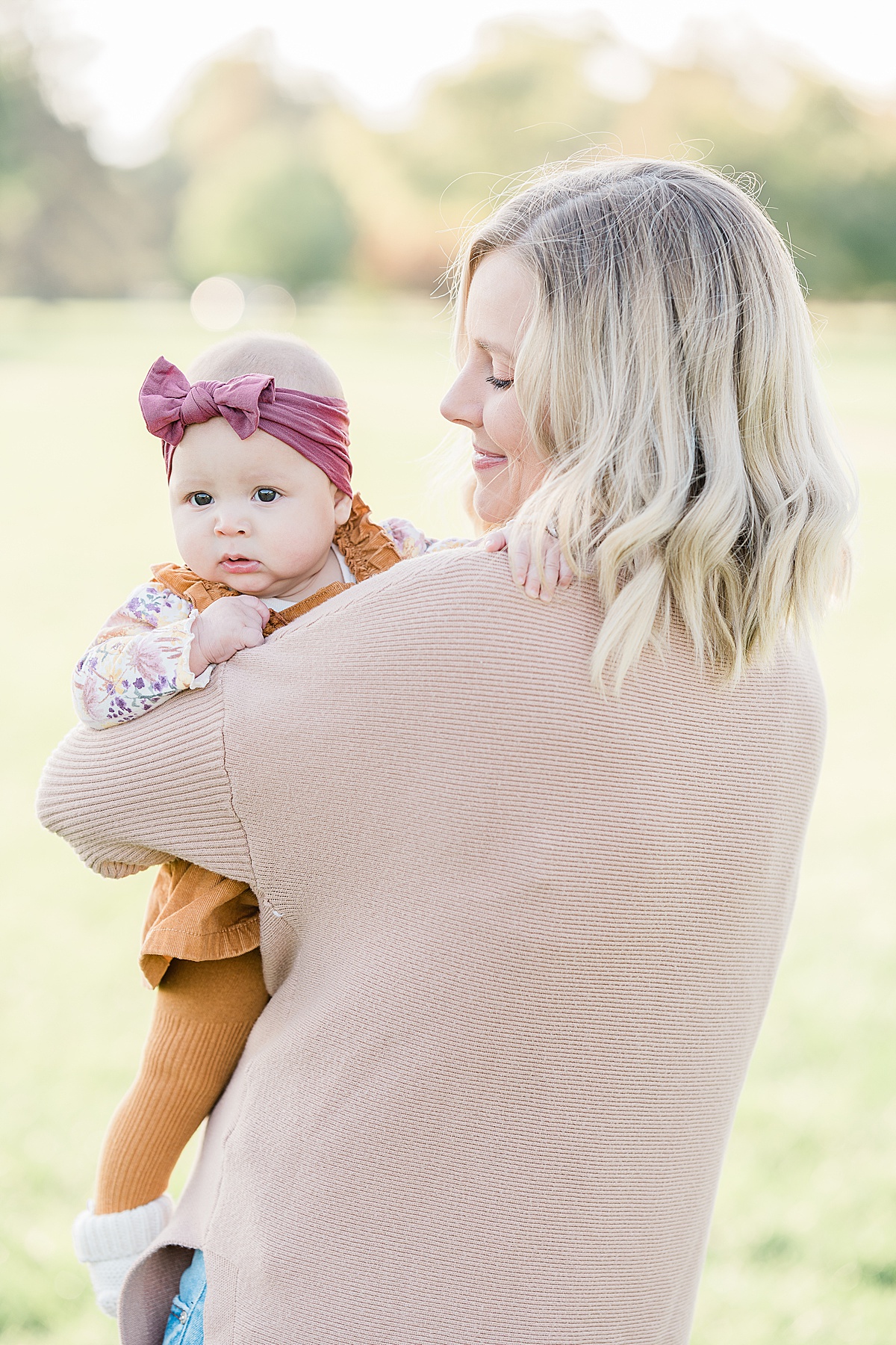 Woman in pink sweater holding a baby in orange jumpsuit and pink headband