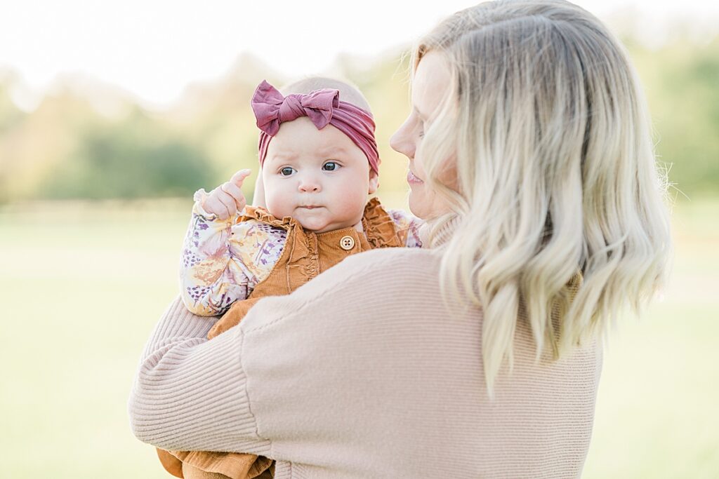 Woman in pink sweater holding a baby in orange jumpsuit and pink headband