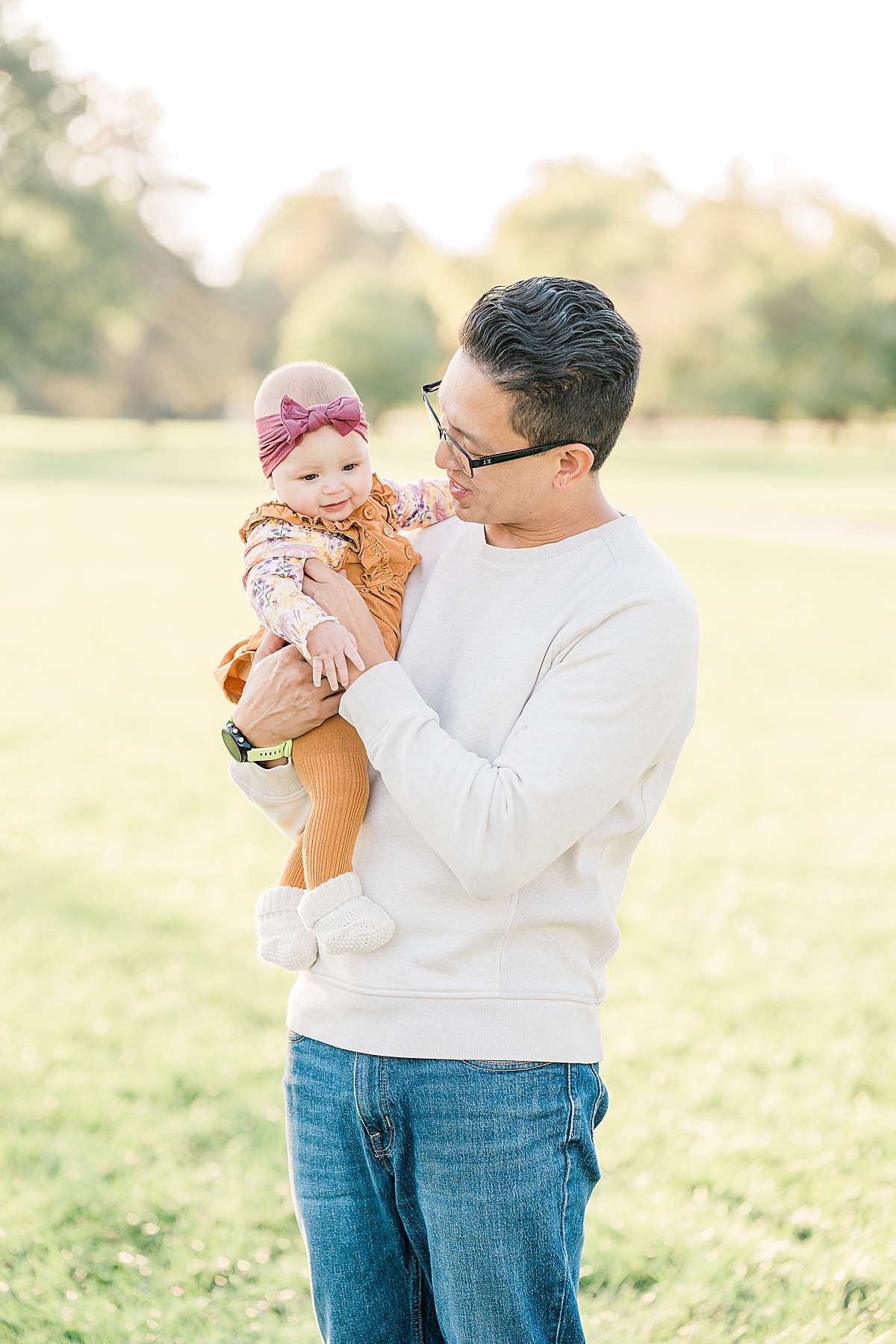 Man in white sweater holding baby in orange jumpsuit and pink headband