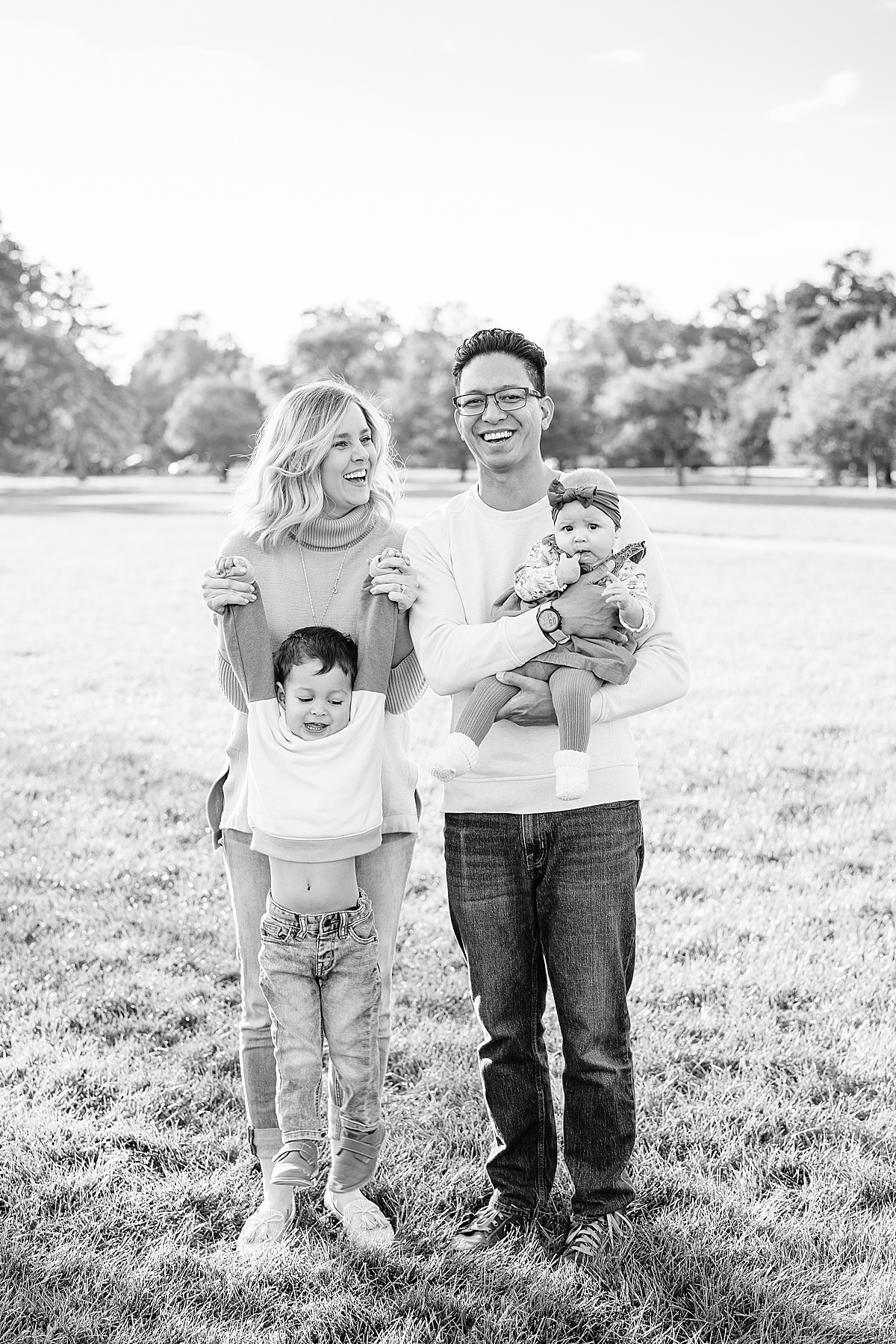 Black and white photo of one man and one woman laughing at each other while holding baby and toddler